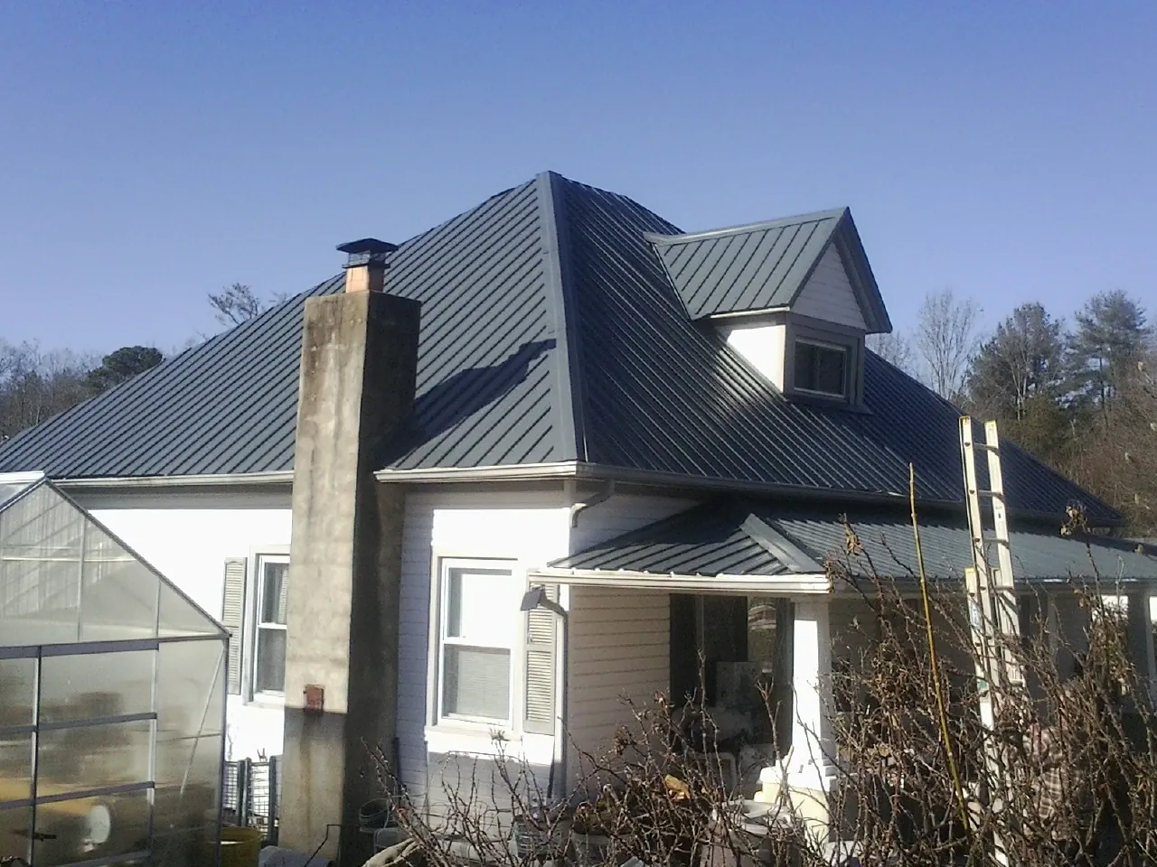 Dark blue standing seam metal roof on a white farmhouse with dormer — Slate & Tile Roof Repair by Roofing Brothers in Fort Bridger