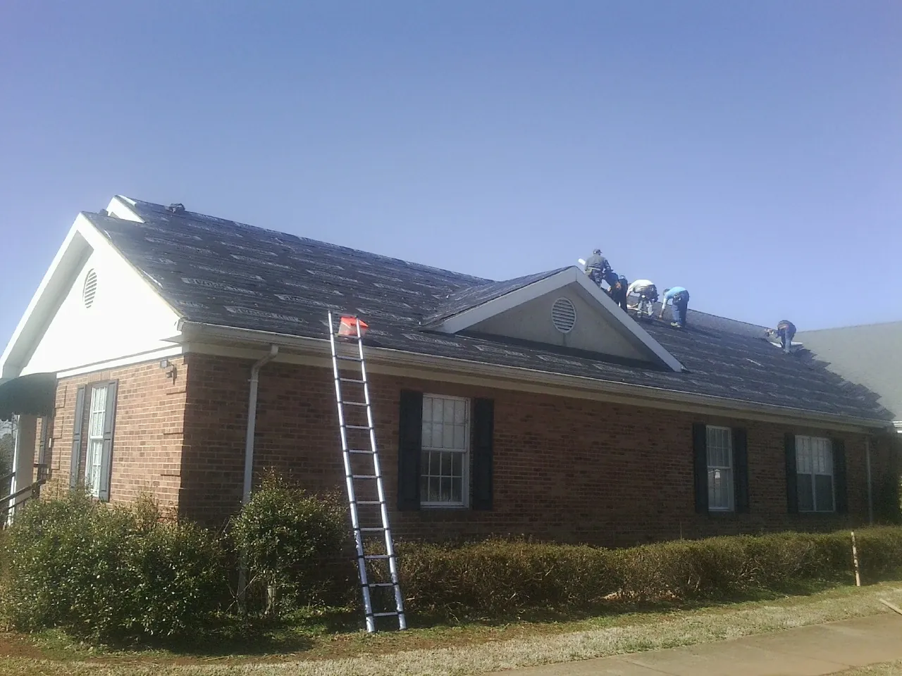 Crew tearing shingles off a brick ranch roof with a ladder set — Emergency Roof Repair work by our crew in Fort Bridger