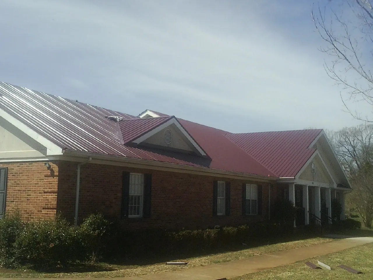 Red metal roof with gabled entries on a long brick building, from a Hail Damage Roof Repair job in Fort Bridger