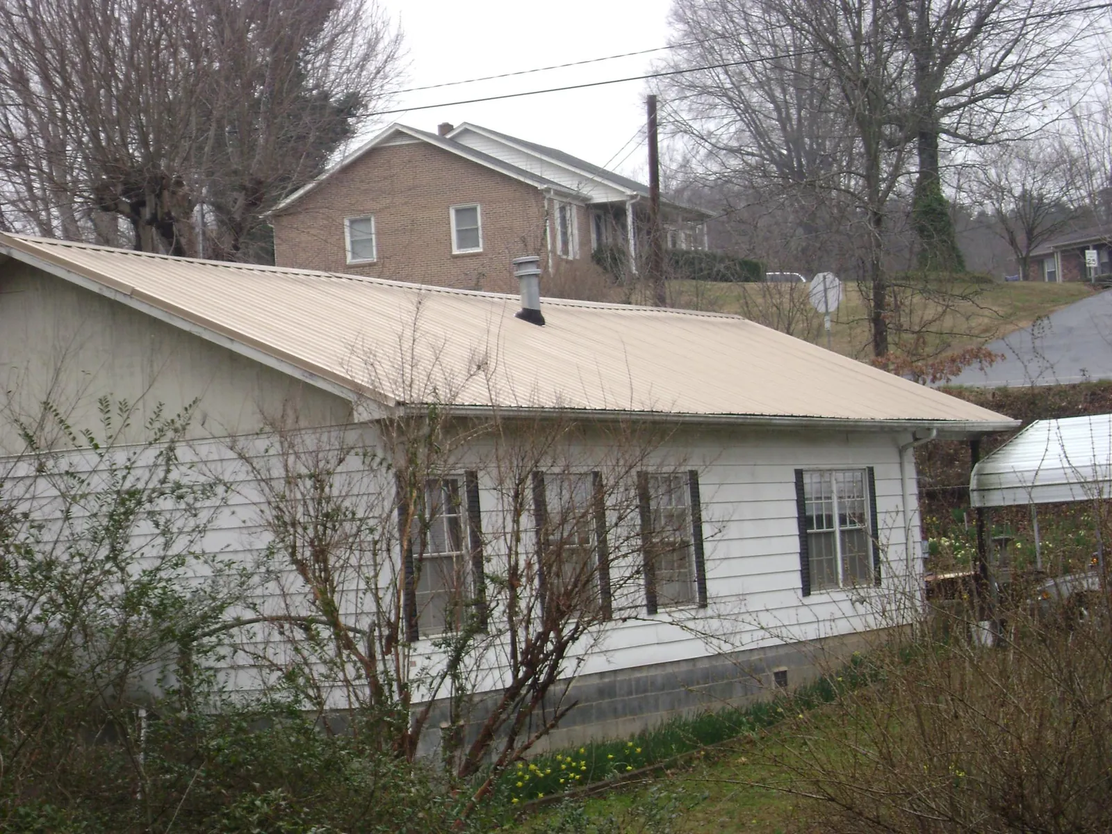 Tan metal roof on a white sided house set into a hillside — Commercial Roofing by Roofing Brothers in Fort Bridger